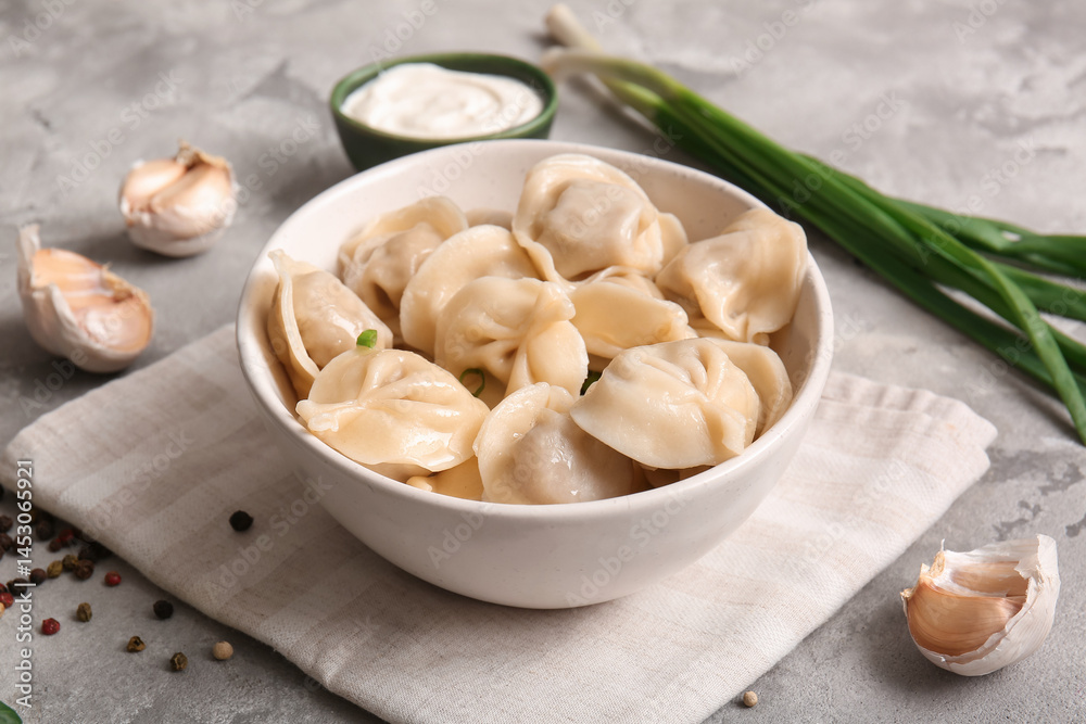 Bowl of delicious boiled dumplings with green onion, garlic and sour cream on grey background, closeup Bowl of delicious boiled dumplings with green onion, garlic and sour cream on grey background, closeup