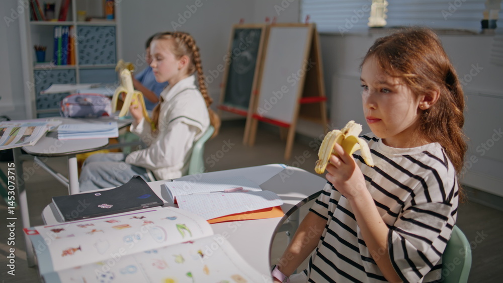 School kids eating bananas at desks closeup. Hungry classmates having lunch