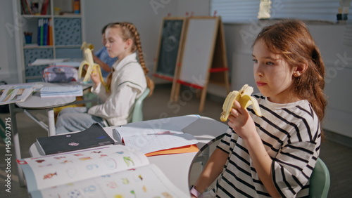 Obraz na płótnie School kids eating bananas at desks closeup. Hungry classmates having lunch w salonie