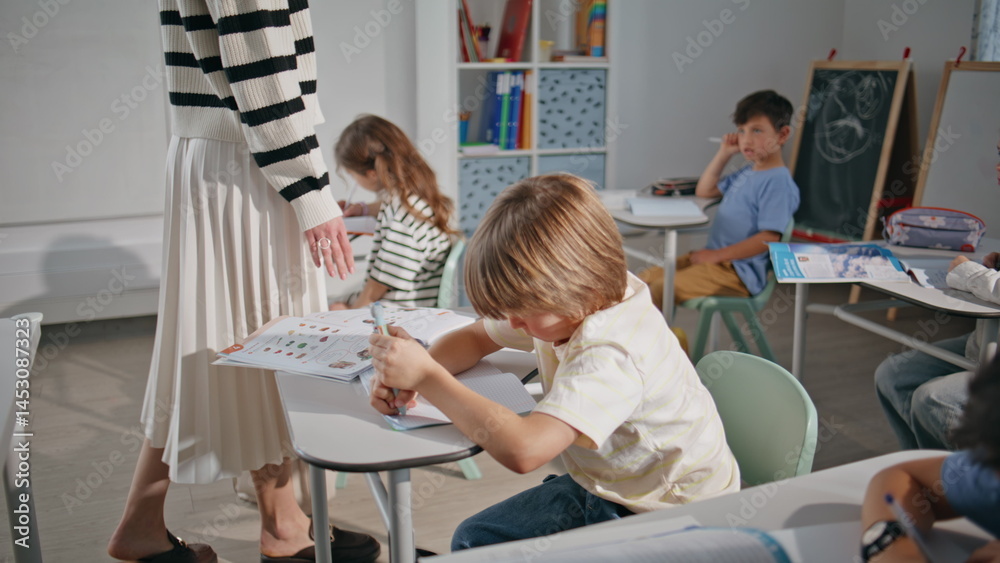 Children group doing test writing notebooks in school closeup. Teacher walking