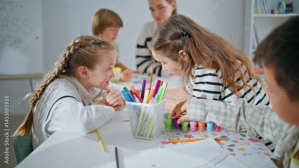 Two girls drawing pictures at big school table closeup. Inspired kids talking