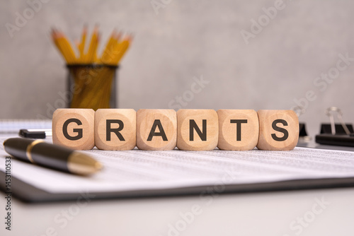 Word GRANTS on wooden blocks with office supplies in background.