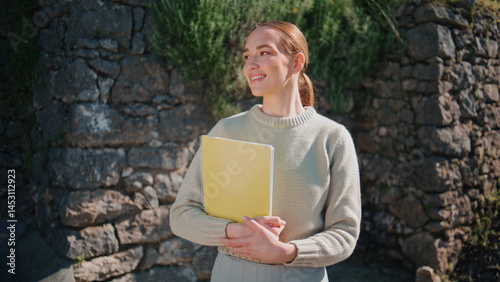 Portrait happy tutor posing in front wall in sun beams. Smiling lady with books