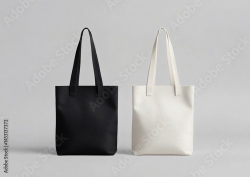 Two plain tote bags, one black and one white, are displayed side by side on a neutral gray background,

 photo