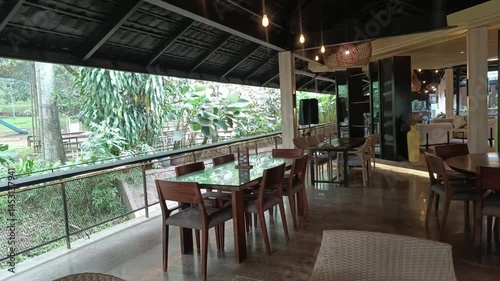 A veranda in a restaurant features a view of the garden and playground with natural light, creating a peaceful and serene atmosphere for dining.