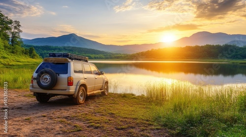 Off-road vehicle parked near a serene lake at sunset mountains and golden sun providing a picturesque landscape. The vehicle is illuminated in the golden hour with spare tire attached.