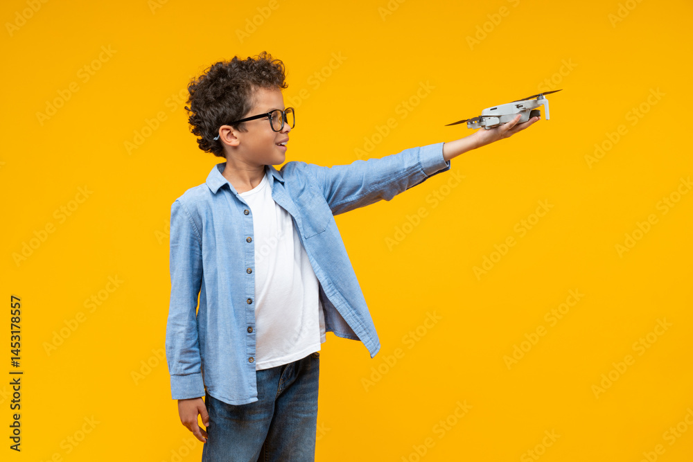 © wpadington - Portrait of casually dressed African American kid student posing in studio holding generic design drone in his hand, isolated over bright colored orange yellow background