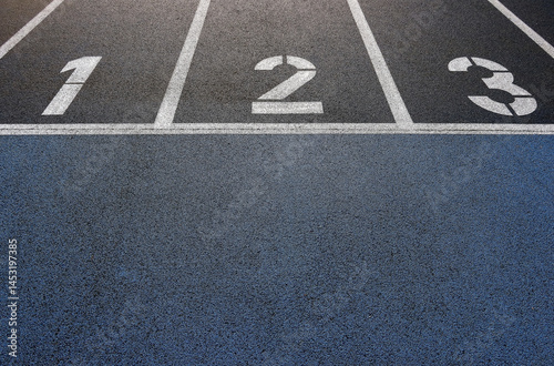 Running track with lane numbers 1, 2, and 3 in afternoon sunlight, close-up view of textured surface and painted lines on blue and black asphalt, concept of race, competition and fitness