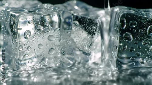 Close up view of melting ice cubes with water droplets on a reflective surface in dark setting