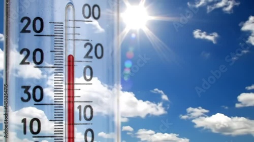 Close up of a thermometer showing a high temperature against a blue sky with clouds view