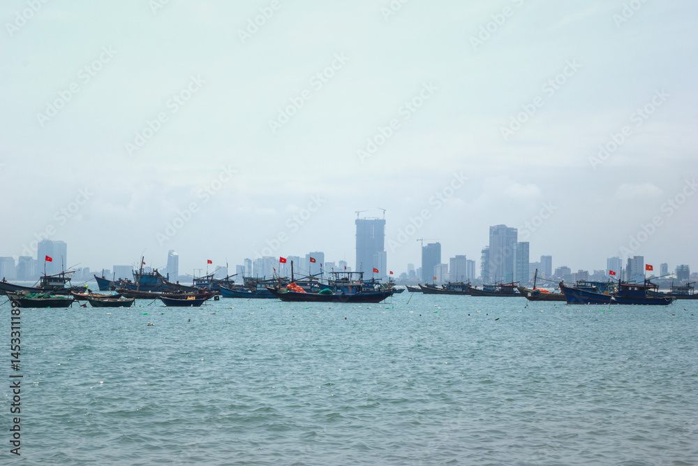 Naklejka premium Small fishing boat sailing on calm sea with a large city skyline in the foggy. Danang, Vietnam.