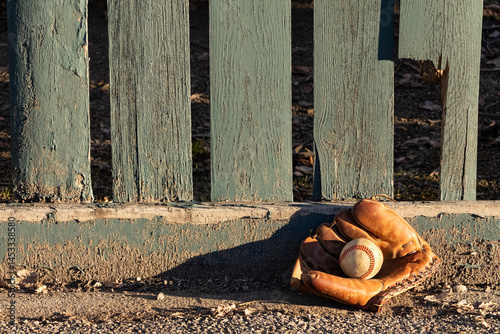 Принти на полотні Outdoor baseball and mitt resting against a green wooden fence