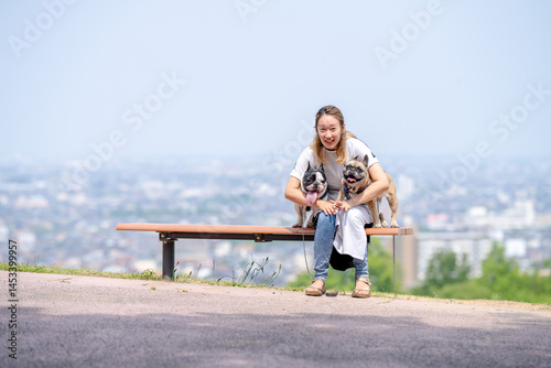 Obraz na płótnie On a summer morning in a park with blooming hydrangeas, a Japanese woman in her 30s walks two French Bulldogs. They sit on a hilltop bench, overlooking the city, with flowers and greenery all around. w salonie