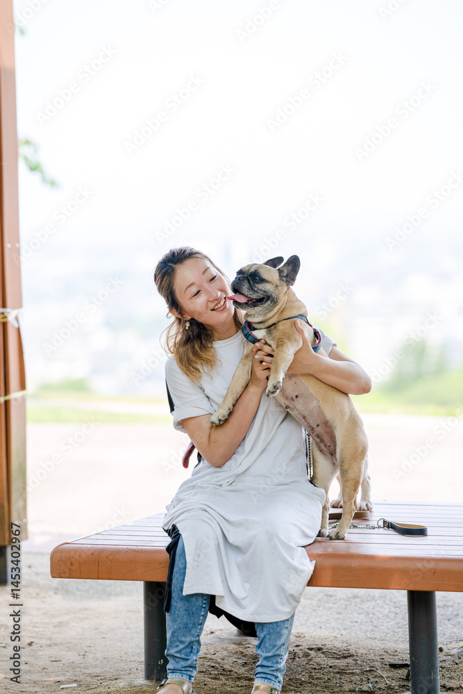 On a summer morning in a park with blooming hydrangeas, a Japanese woman in her 30s walks two French Bulldogs. Sitting on a bench, they share a moment, surrounded by flowers and early summer greenery