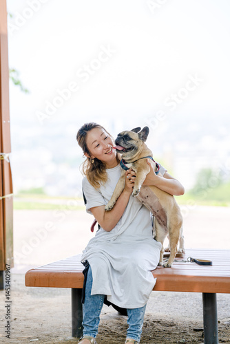 Obraz na płótnie On a summer morning in a park with blooming hydrangeas, a Japanese woman in her 30s walks two French Bulldogs. Sitting on a bench, they share a moment, surrounded by flowers and early summer greenery w salonie