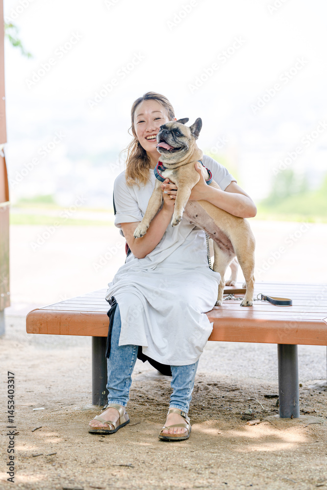 On a summer morning in a park with blooming hydrangeas, a Japanese woman in her 30s walks two French Bulldogs. Sitting on a bench, they share a moment, surrounded by flowers and early summer greenery