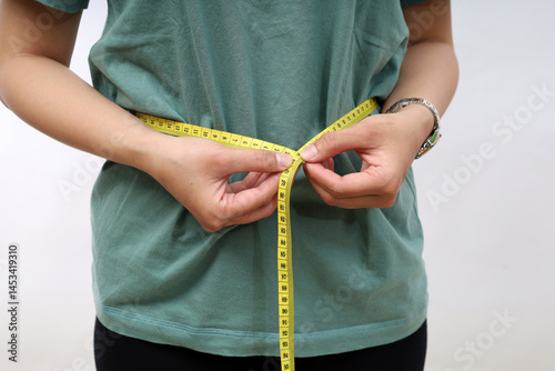 Close up woman in green t-shirt measuring her waist with yellow measuring tape. Weight loss, slim body, healthy lifestyle concept. Figure control and counting calories. Successful diet plan.