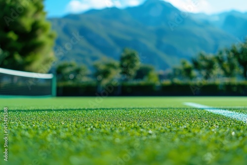 Obraz na płótnie Closeup of vibrant green grass on a tennis court with mountains in the background during a sunny day, Closeup of green grass on a tennis court with a white line and blurred background w salonie