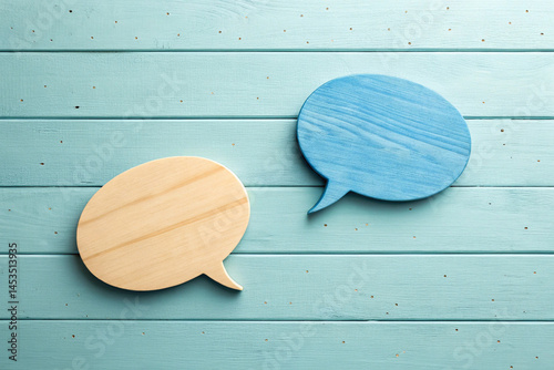 Two wooden speech bubbles, one natural wood and one blue, resting on a wooden background The image represents communication, dialogue, or discussion in a simple and modern way