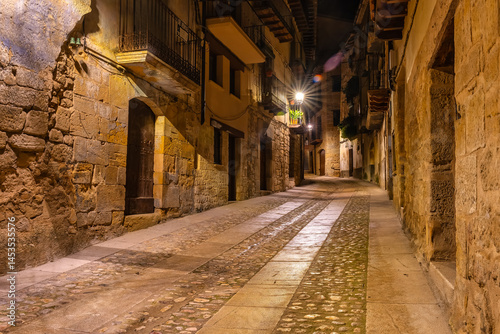 Obraz na płótnie Alley with medieval stone houses at night lit with street lamps, Valderrobles, Teruel. w salonie