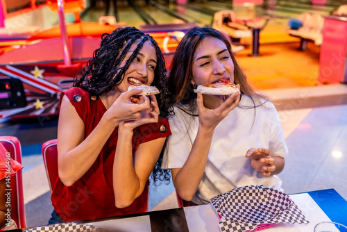 Multiethnic female friends eating pizza at bowling alley
