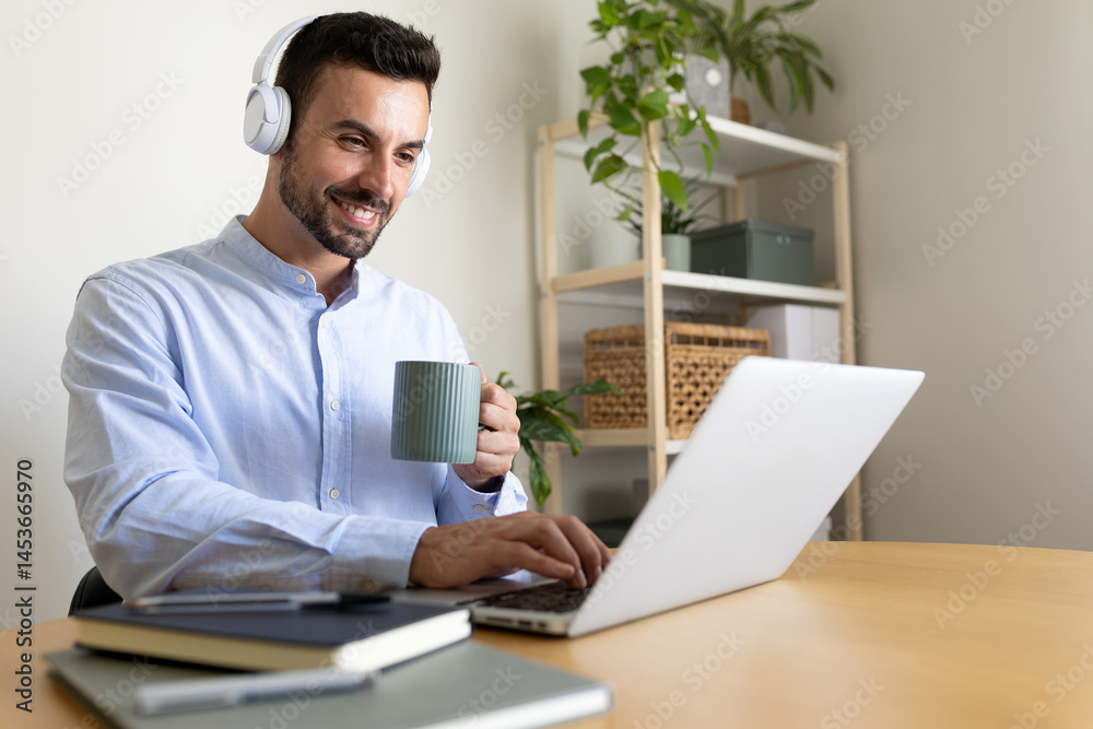 Fototapeta premium Caucasian man with headphones working at home office. Happy male entrepreneur using laptop.