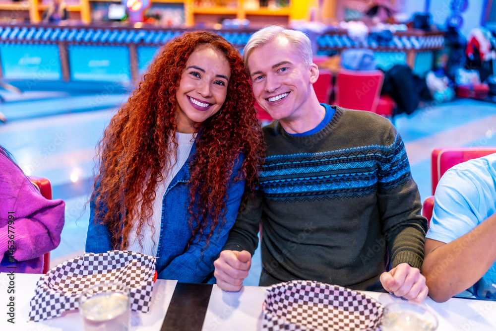 Happy multiethnic friends enjoying meal at bowling alley restaurant