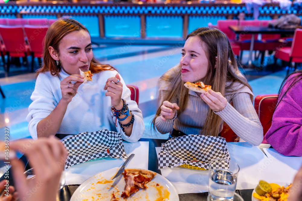 Cheerful young women eating pizza at bowling alley restaurant