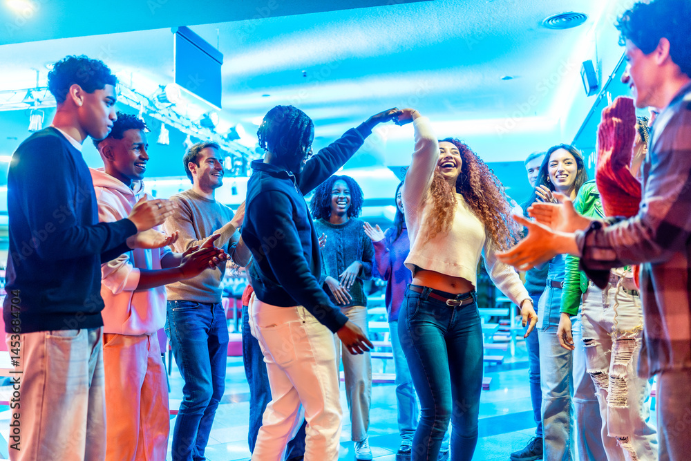 Happy multiethnic friends dancing and clapping at bowling alley