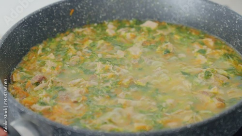 A pot filled with boiling soup contains chunks of meat and vibrant vegetables