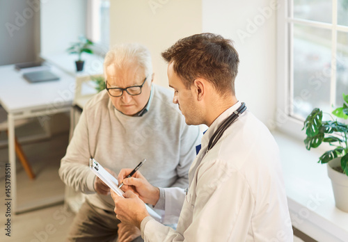Portrait of a senior elderly gray-haired man patient in medical office listening to male doctor holding report file with appointment and giving consultation during medical examination in clinic.