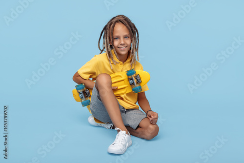 Stylish boy with african dreads with skateboard posing over blue background