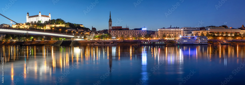 Bratislava, Slovakia. Wide angle panoramic city skyline reflecting in water of Danube river at dusk