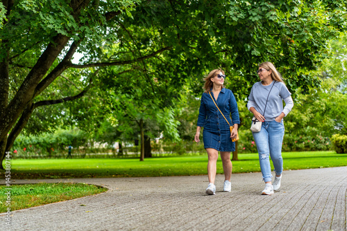 Two happy middle aged women walking in city park. Meeting of friends in park. Front view