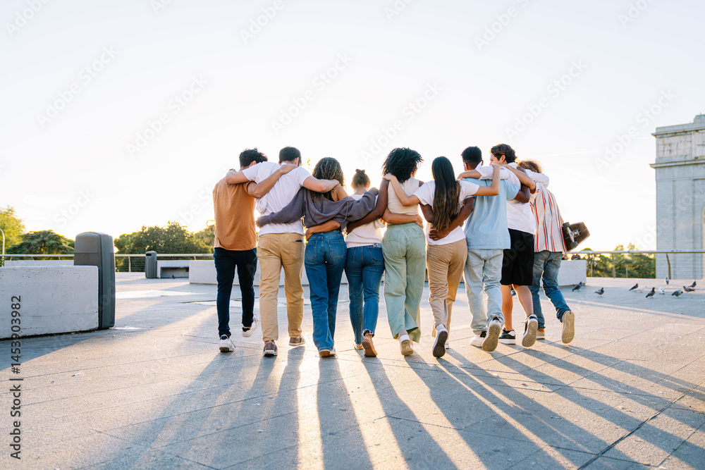 Obraz premium Diverse group of students walking together on a campus rooftop, arms around each other, celebrating friendship and unity against a sunset backdrop