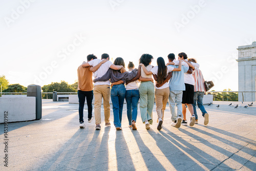 Diverse group of students walking together on a campus rooftop, arms around each other, celebrating friendship and unity against a sunset backdrop