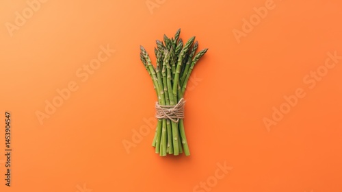 Green asparagus bundle tied with jute rope on a vivid orange backdrop