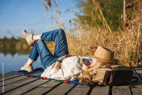 Obraz na płótnie Woman relaxing and napping on pier at lake, face covered by straw hat