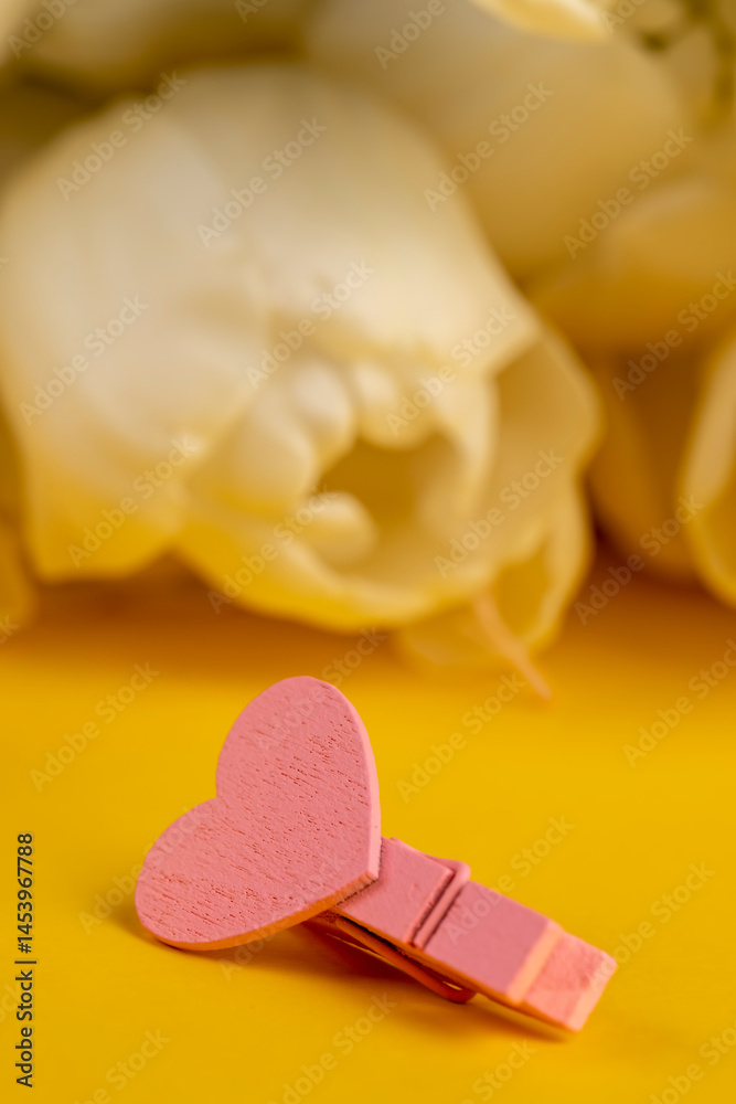 white tulips on yellow paper, a clothespin with a decorative heart made of plywood, close up