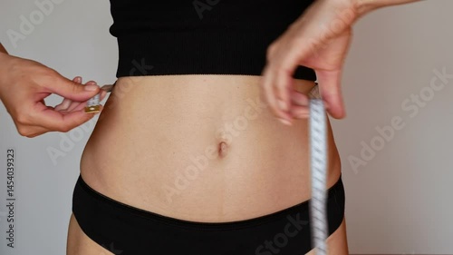 Close-up, a girl with a trim figure measures her waist after losing weight, showing off her slim body and flat stomach.