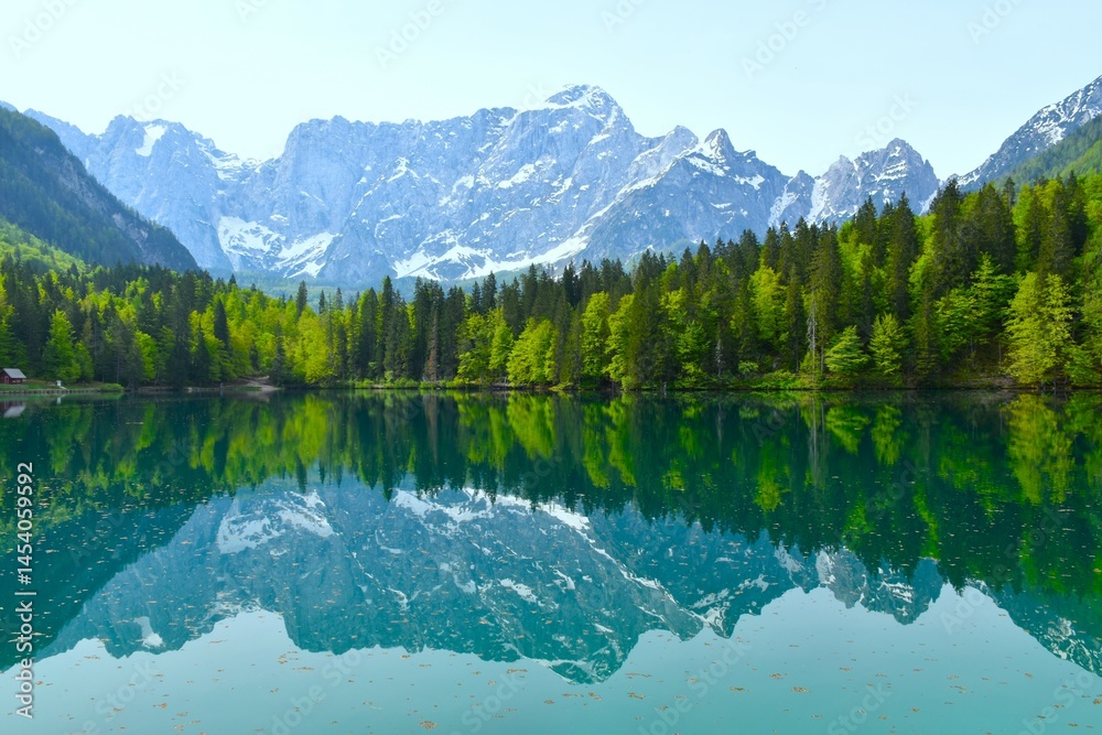 View of mountain Mangart above lago di fusine inferiore with a forest at the lake shore in municipality of Tarvisio, Italy