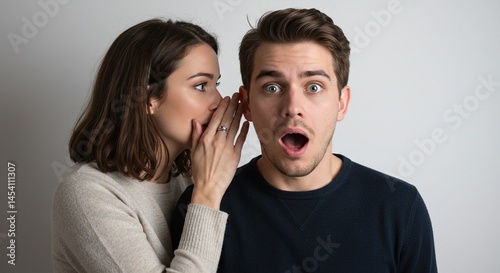 A woman whispers secret into a man's ear. The man's expression is one of shock and surprise, with wide eyes and open mouth.