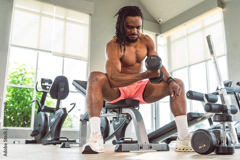 Obraz premium A man is lifting weights in a gym. There are several pieces of gym equipment in the background, including a stationary bike, a bench, and a weight rack