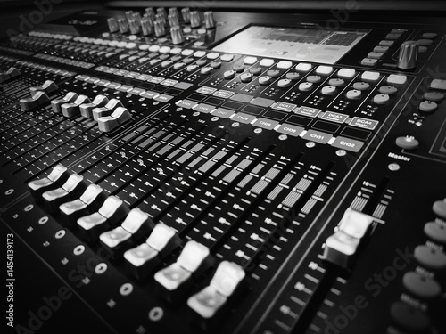 Close-up of a professional audio mixing console in black and white, showing detailed faders, knobs, and controls used in sound engineering and music production.
