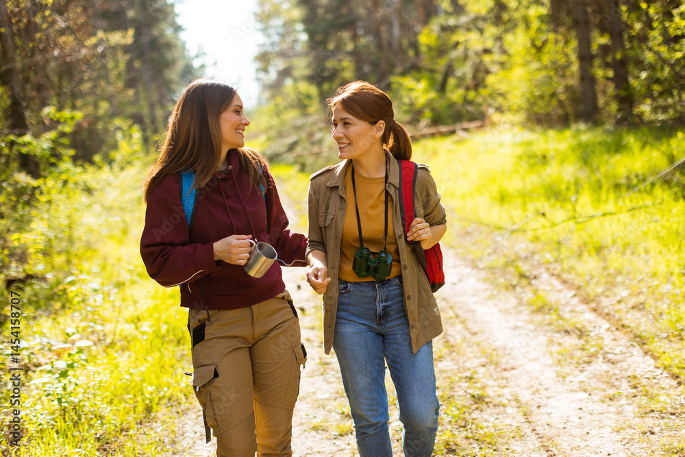 Two friends enjoy a joyful hike through a sunlit forest path on a warm spring day in nature's embrace