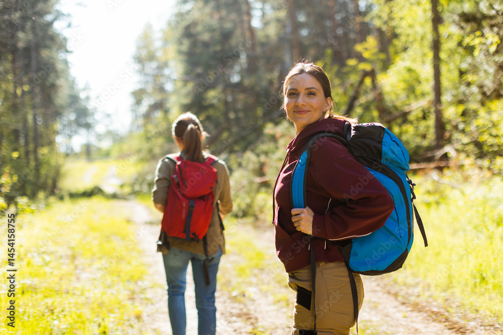 Exploring the serene wilderness, two friends embark on an adventurous hiking journey in a vibrant green forest during a sunny afternoon
