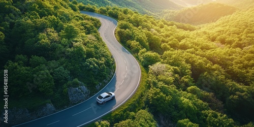Obraz na płótnie A winding road through a lush green forest during sunset, with a car driving on the asphalt surface. w salonie