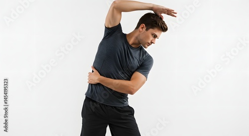 Man in gray shirt stretching sideways with hand on ribs against a white background in studio shot