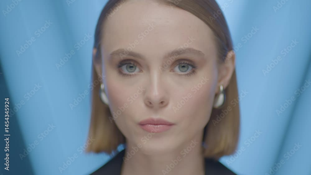 A charismatic young woman looking directly at the camera in a studio with a blue background. Strong expression, professional appearance, and modern aesthetic. A charismatic young woman looking directly at the camera in a studio with a blue background. Strong expression, professional appearance, and modern aesthetic.