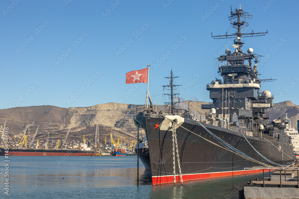 Fototapeta premium The museum ship is moored at the eternal parking lot in the port of Novorossiysk. A Soviet cruiser in the port. A warship with cannons. A large warship at the pier.